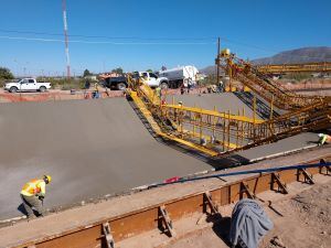 Construction workers and large equipment working on cement in a large ditch