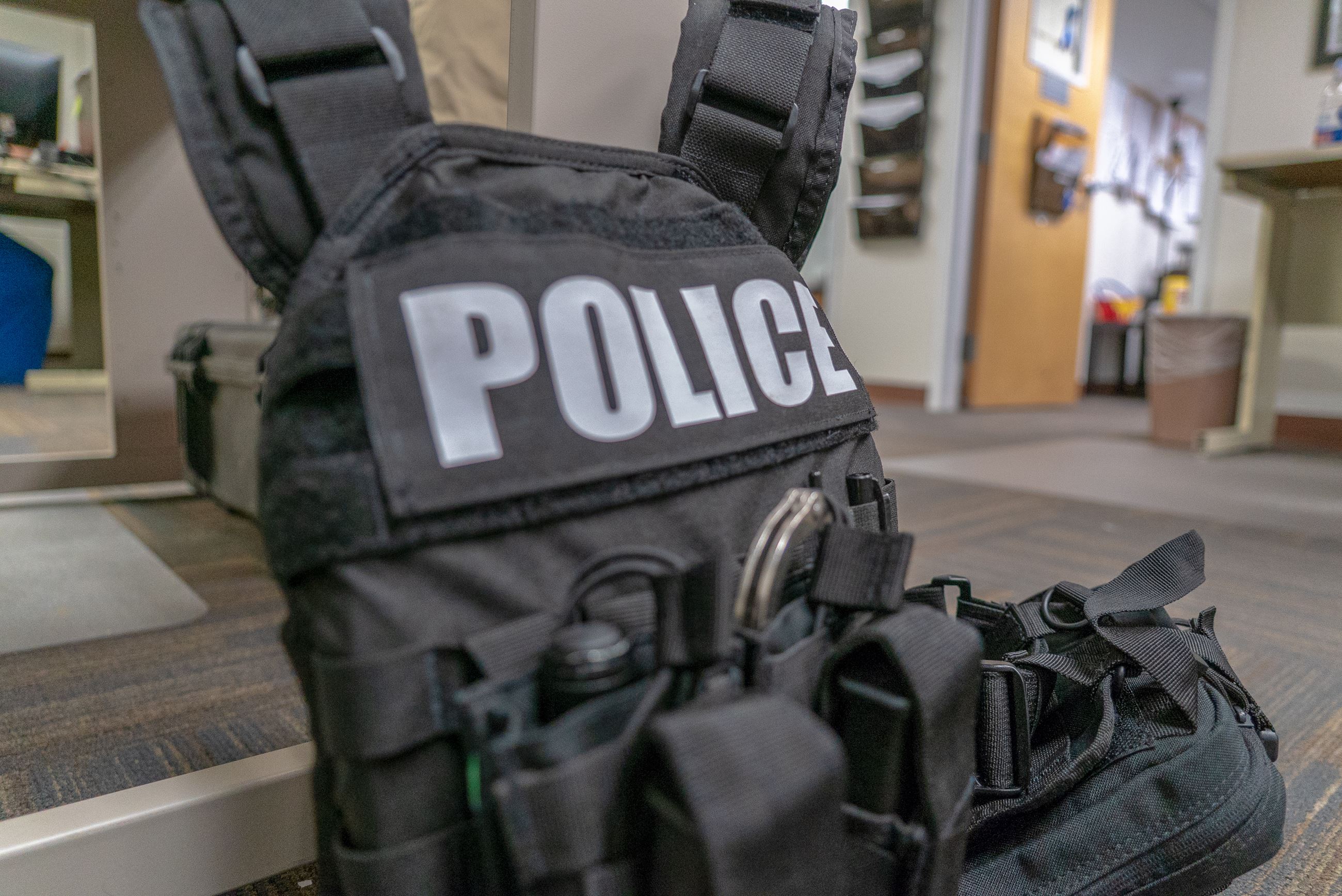 A black police vest sits on the floor in an office.