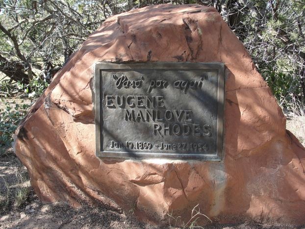 Rhodes' large stone and bronze grave marker is shaded by pinon trees.